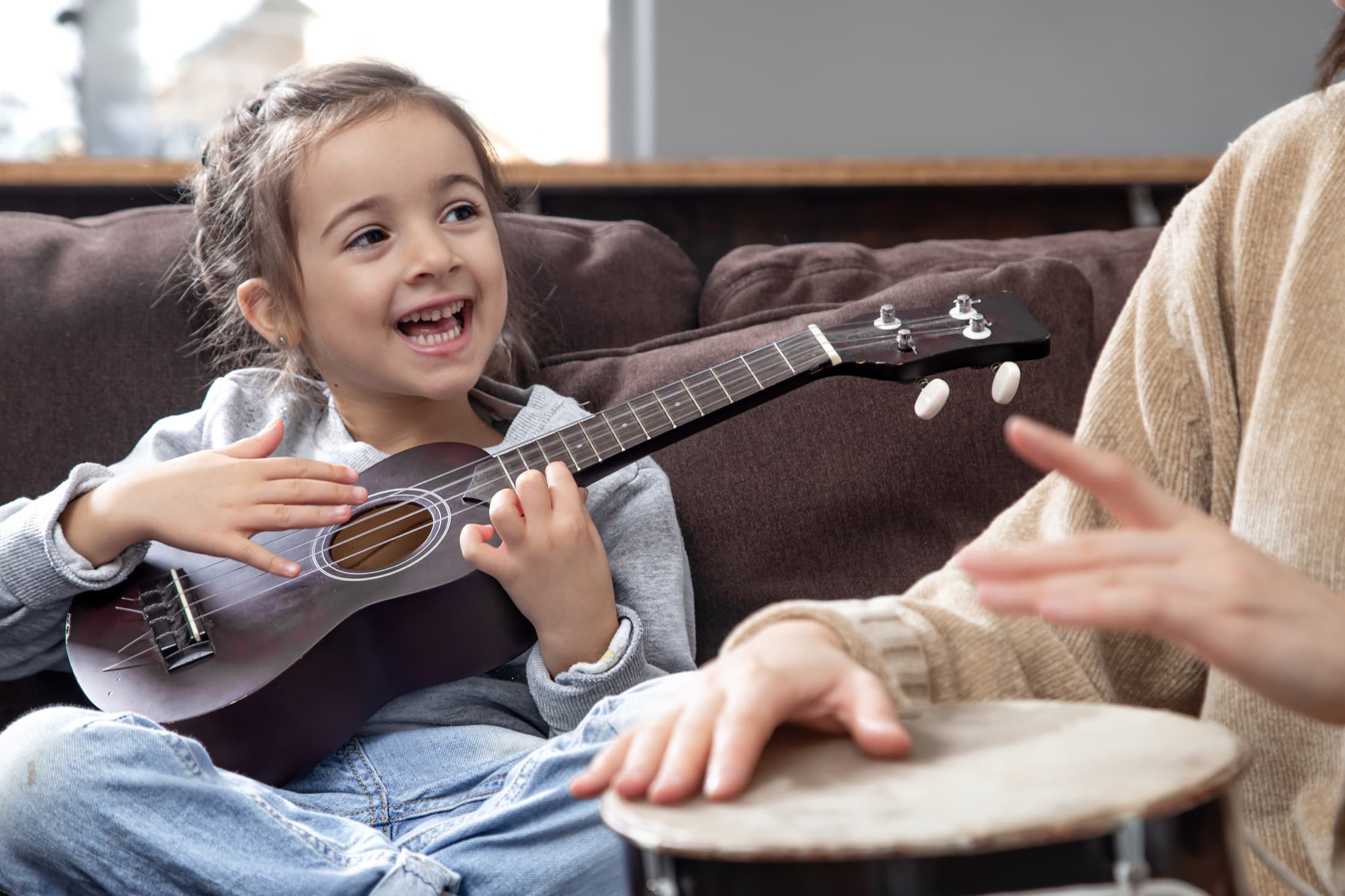 Criança sorrindo em experiência musical com ukulele e acompanhamento próximo